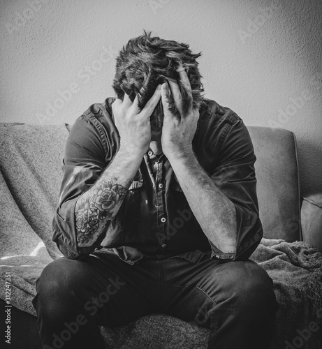 Distressed Man Sits on Couch with Head in Hands