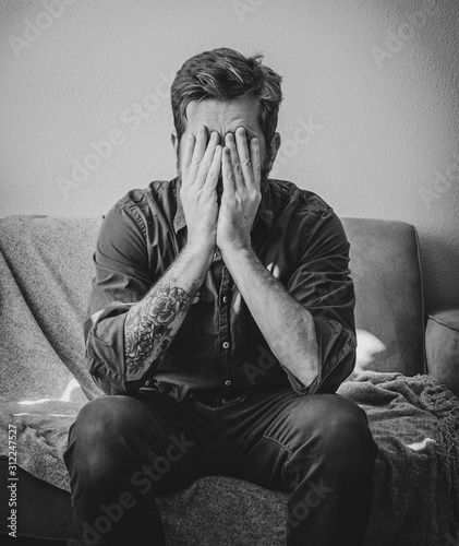 Distressed Man Sits on Couch with Head in Hands