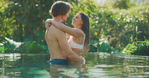 Happy diverse couple embracing and kissing in a beautiful jungle swimming pool on their tropical vacation together photo