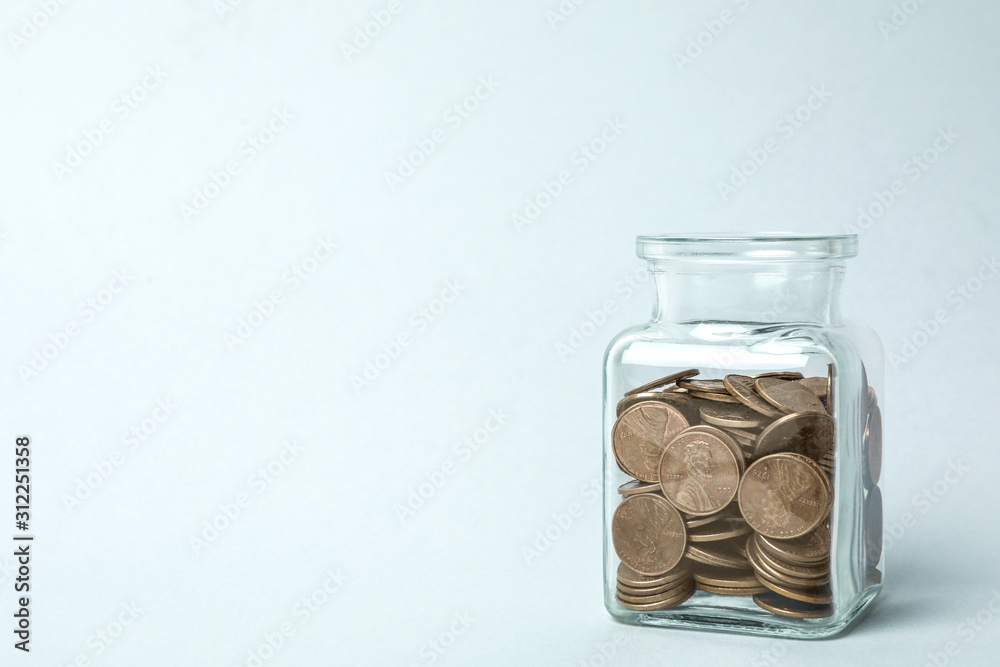 Glass jar with coins on light background, space for text Glass jar with coins on light background, space for text