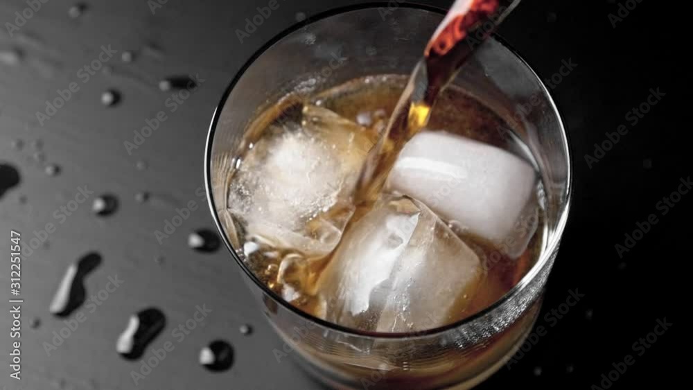 Pouring Cola in glass with ice on black table overhead shot Pouring Cola in glass with ice on black table overhead shot