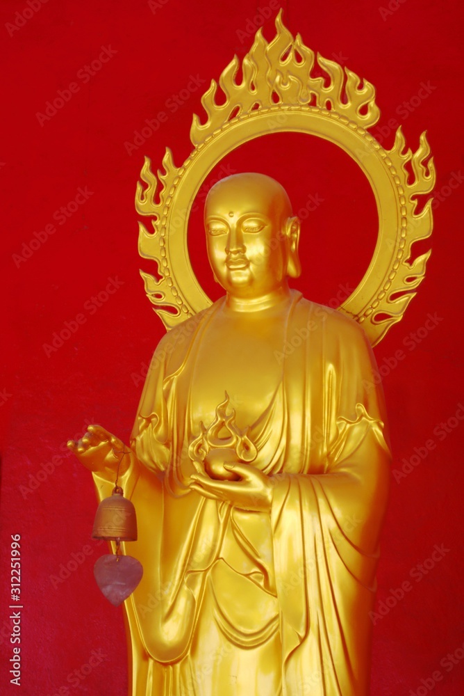 Golden buddha against a red wall at a temple in Phuket, Thailand.