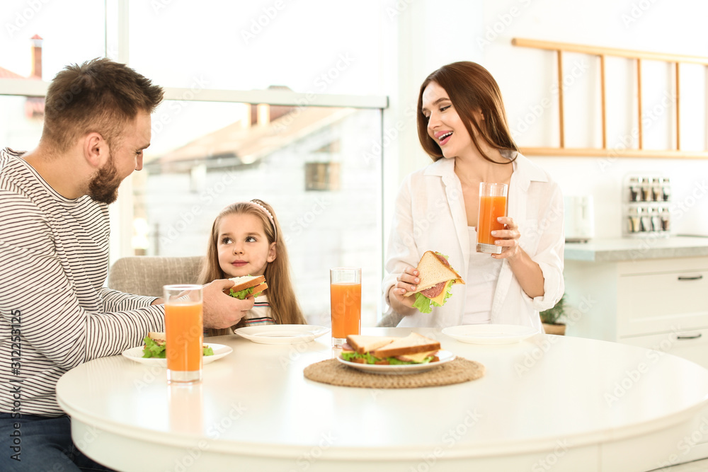 Happy family having breakfast with sandwiches at table in kitchen Happy family having breakfast with sandwiches at table in kitchen