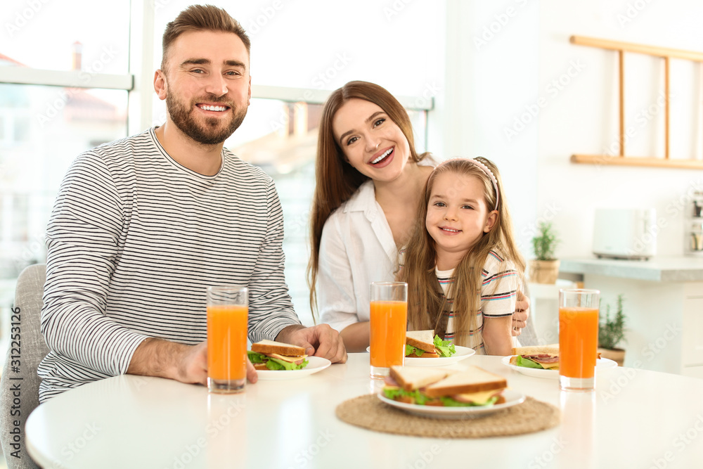 Happy family having breakfast with sandwiches at table in kitchen Happy family having breakfast with sandwiches at table in kitchen