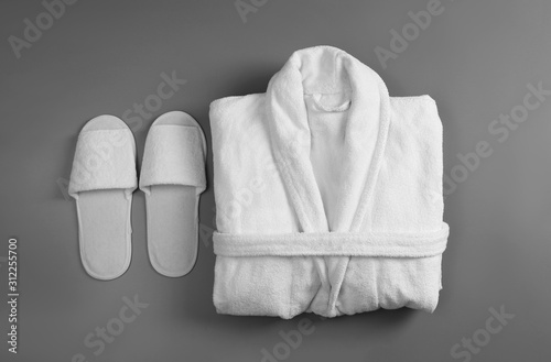 Clean folded bathrobe and slippers on grey background, flat lay photo