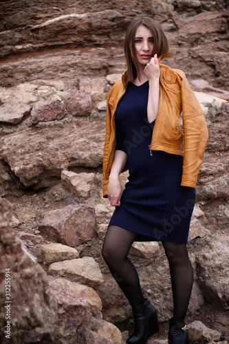 Beautiful girl standing near the rocks in a yellow jacket