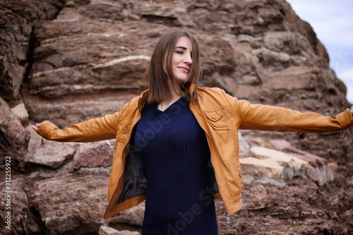 Beautiful smiling girl in a yellow jacket stands against a stone wall