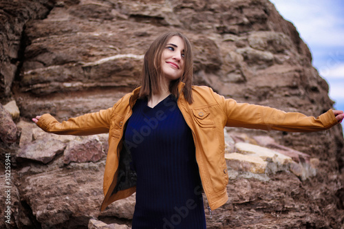 Image of happy girl in yellow jacket smiling while sitting by rock in morning