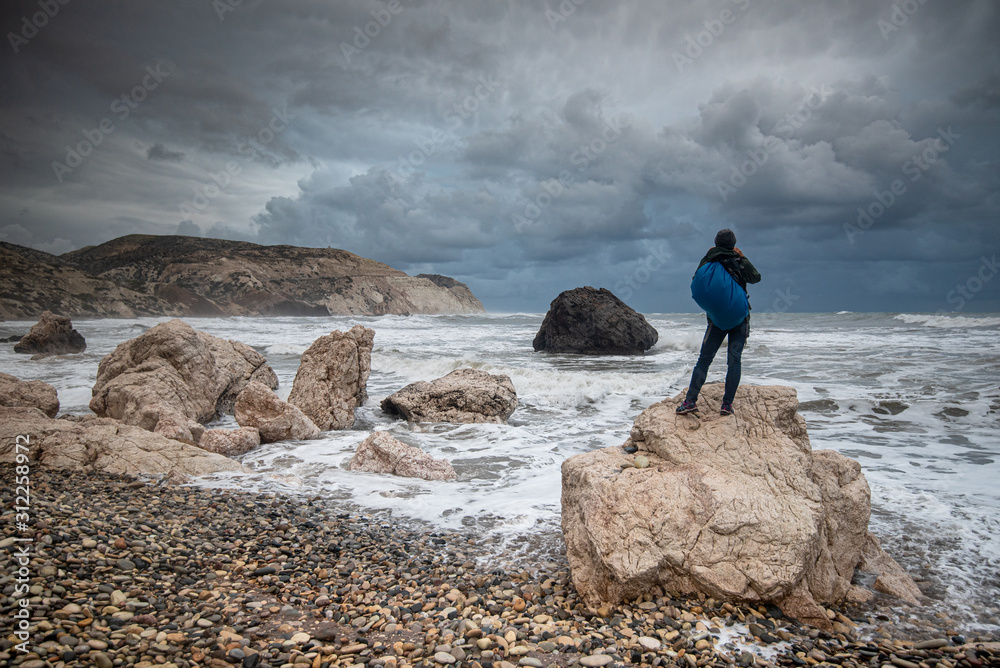 Obraz premium Unrecognised person standing at the rock and enjoying the stormy seascape
