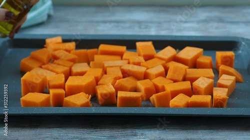 Chopped pumpkin being drizzled with olive oil before baking on a tin. Female hands