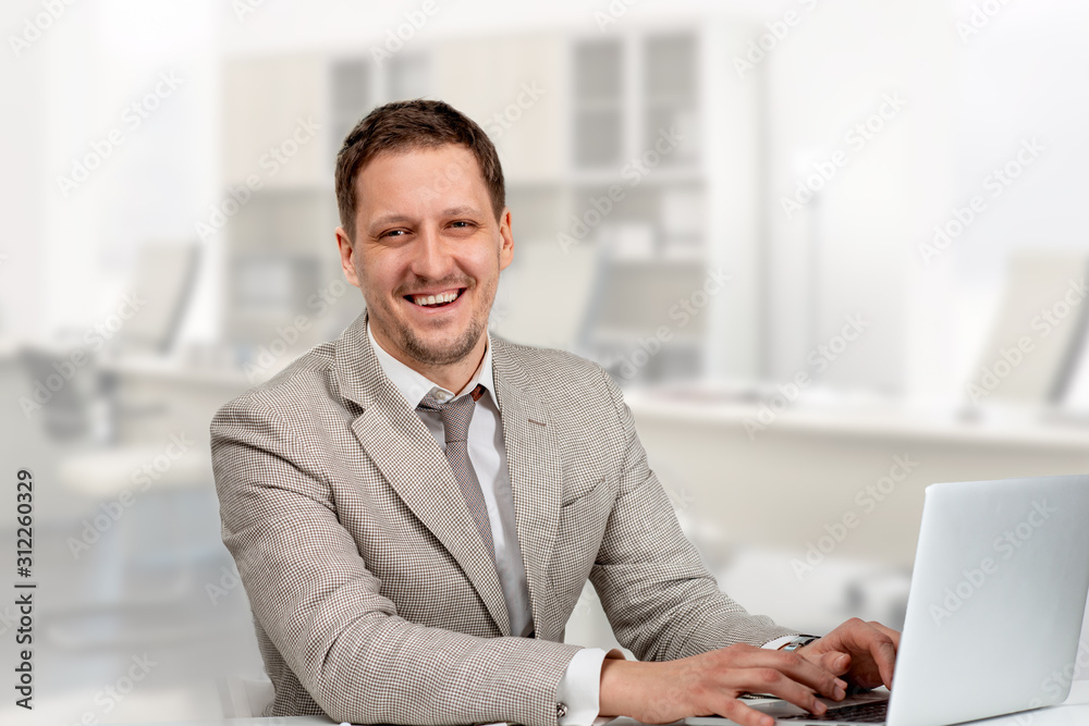 Shot of smiling man wearing a beige jacket and a tie working on a laptop in ofice. Shot of smiling man wearing a beige jacket and a tie working on a laptop in ofice.