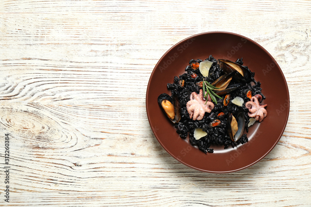 Delicious black risotto with seafood on white wooden table, top view. Space for text