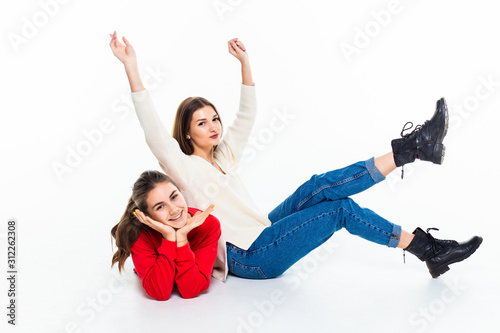 Two teen girl friends have fun sitting on the floor isolated on white background