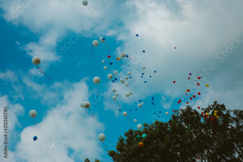 Multicolored balloons pile soaring into the blue sky with white clouds. © Ирина Кусова