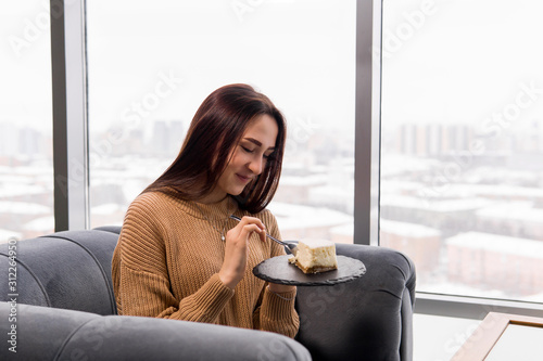 girl eating a cake while sitting in a chair in front of a large window on a winter day