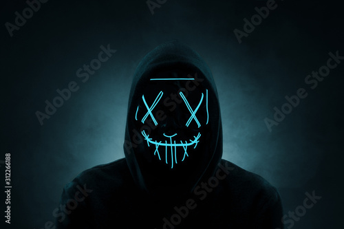 Portrait of an anonymous man, hacker wearing neon mask over dark background photo