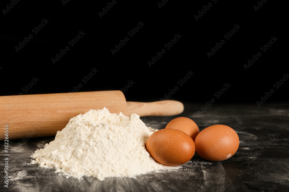 Raw eggs, flour and rolling pin on black background. Baking pie Raw eggs, flour and rolling pin on black background. Baking pie