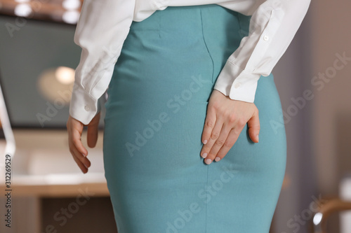 Young woman suffering from hemorrhoid in office, closeup