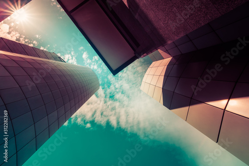 View through modern high rising skyscrapers upwards to blue sky with white clouds. Abstract architecture detail background in turquoise teal blue to burgundy purple pastel colors