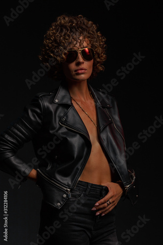 Young attractive sexy girl with curly hair in the form of a rock singer in a leather jacket