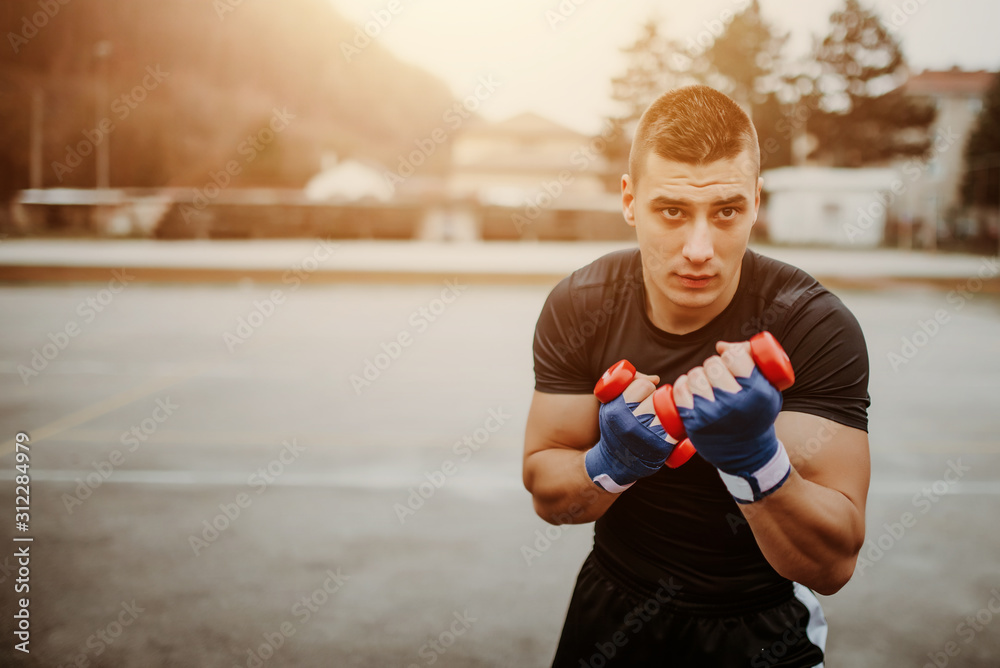 Handsome young man boxer practicing shadow boxing with dumbbells Handsome young man boxer practicing shadow boxing with dumbbells