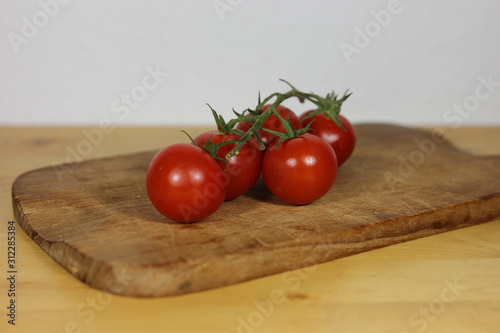 Five tomatoes on a wooden plate with white background close up