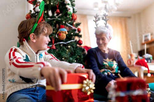 grandmother and grandson by the Christmas tree with gifts from Santa Claus or wise men