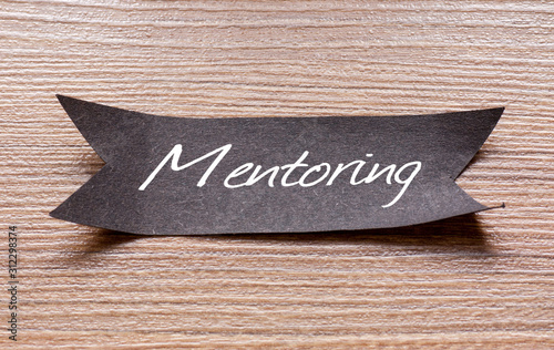 Mentoring word written on Black papper with wooden background