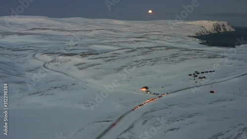 A convoy of cars waiting to go on an icy road towards the Nordkapp, Norway during the midwinter solstice. High angle shot with a full moon. photo