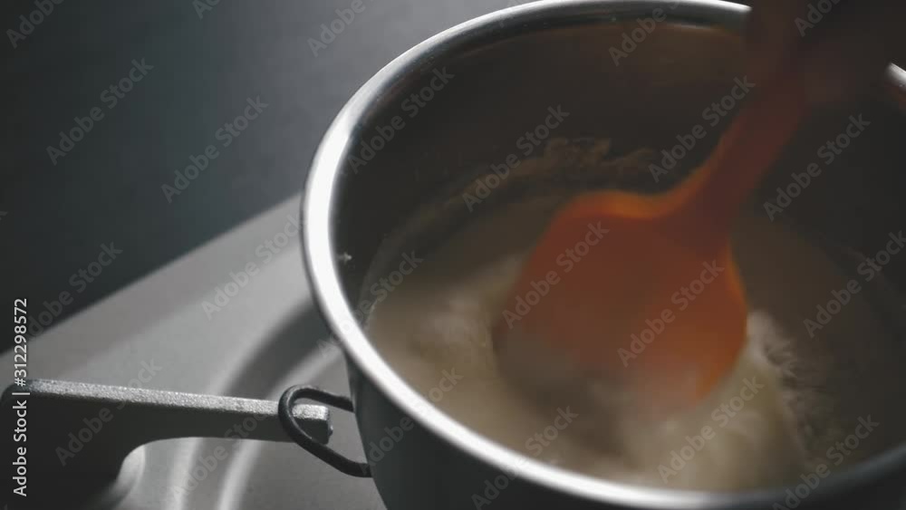 Mixing flour and milk with a polyester spoonin a sause pan on gaz range. close up shot. Mixing flour and milk with a polyester spoonin a sause pan on gaz range. close up shot.