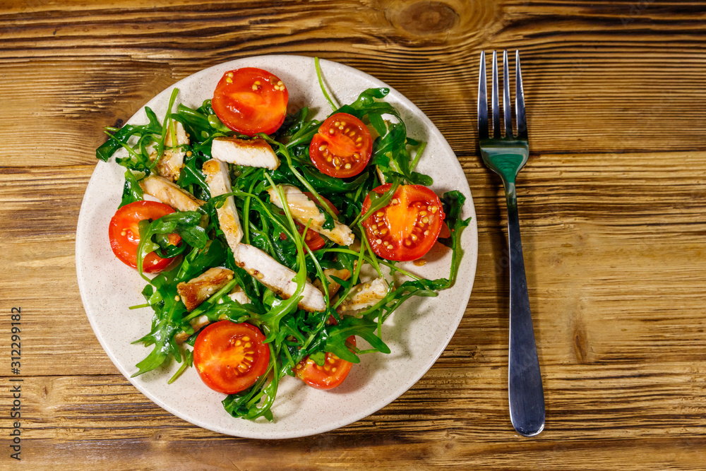 Tasty salad of fried chicken breast, fresh arugula and cherry tomatoes on wooden table. Top view Tasty salad of fried chicken breast, fresh arugula and cherry tomatoes on wooden table. Top view