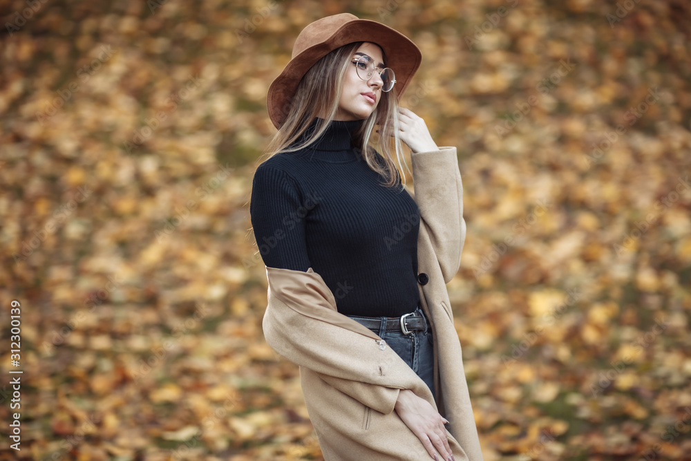 Image-shot of a young attractive woman wearing a coat and felt hat on blurry background of fallen leaves in the autumn park Image-shot of a young attractive woman wearing a coat and felt hat on blurry background of fallen leaves in the autumn park