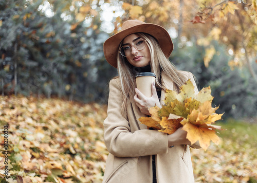 Young funny woman dressed in a coat and hat holds an armful of fallen leaves in the autumn park. Autumn fun