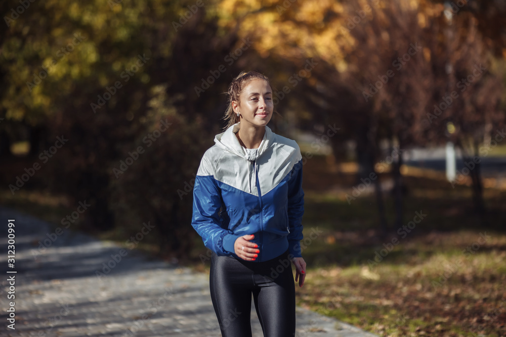 Jogging through the autumn park. Young fit woman in sportswear running outdoors in city park Jogging through the autumn park. Young fit woman in sportswear running outdoors in city park