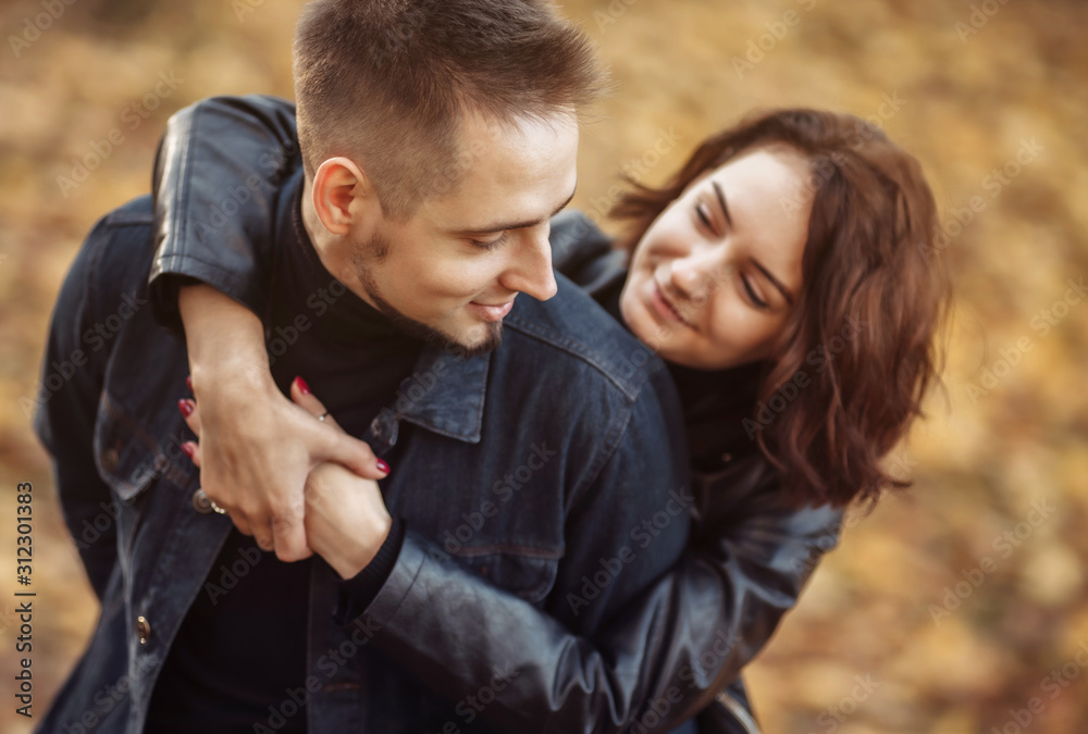 Fototapeta premium Portrait of a young hugging couple of lovers on a blurry background of fallen autumn leaves in the park.