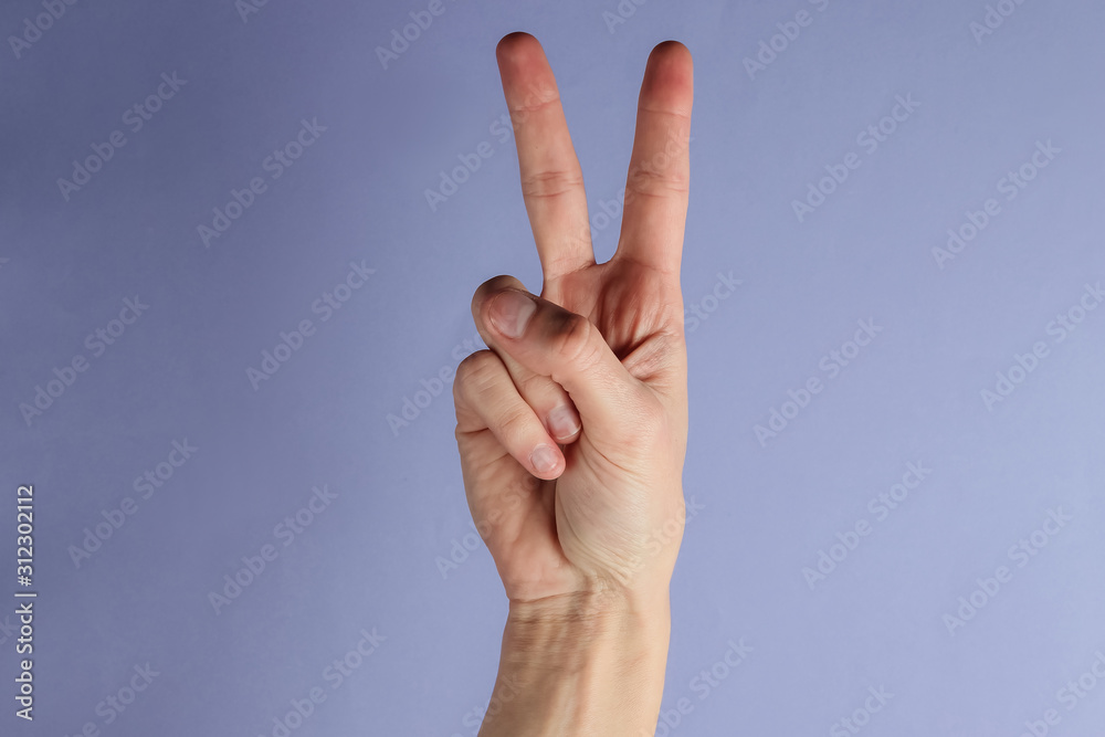 Female hand shows gesture v symbol on purple background Female hand shows gesture v symbol on purple background
