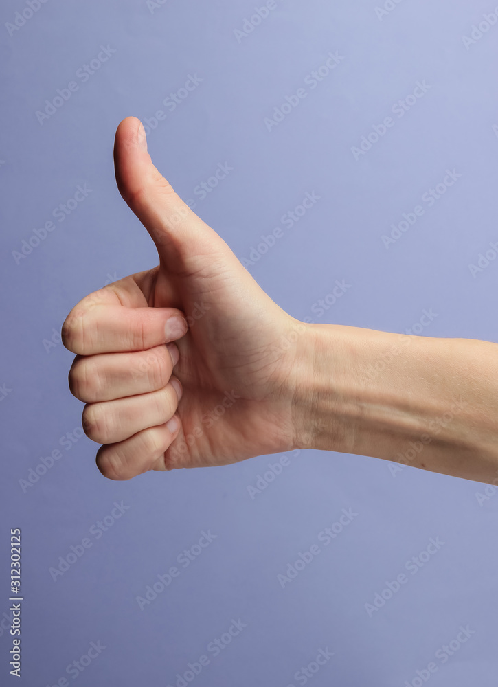 Female hand shows thumb up gesture on purple background Female hand shows thumb up gesture on purple background