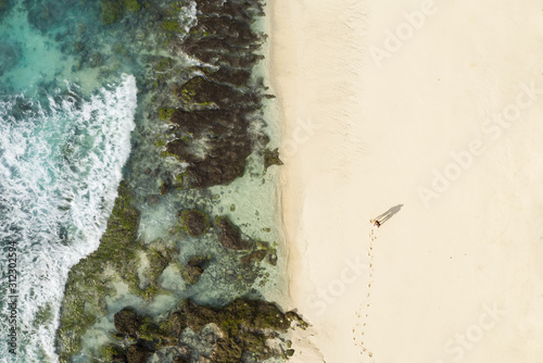 Stunning aerial view of a couple walking on a beautiful beach bathed by a turquoise sea during sunset. Diamond beach, Nusa Penida, Indonesia. 