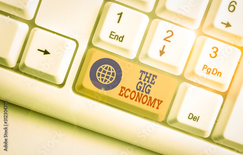 Conceptual hand writing showing The Gig Economy. Concept meaning Market of Shortterm contracts freelance work temporary White pc keyboard with note paper above the white background
