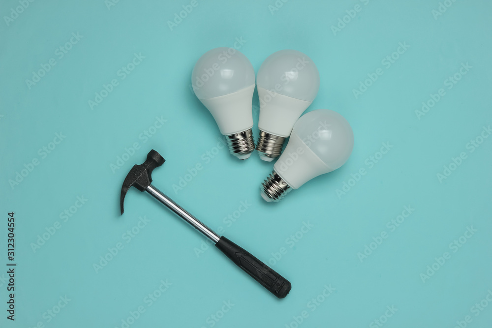 Three LED light bulbs and a hammer on a blue background. Three LED light bulbs and a hammer on a blue background.