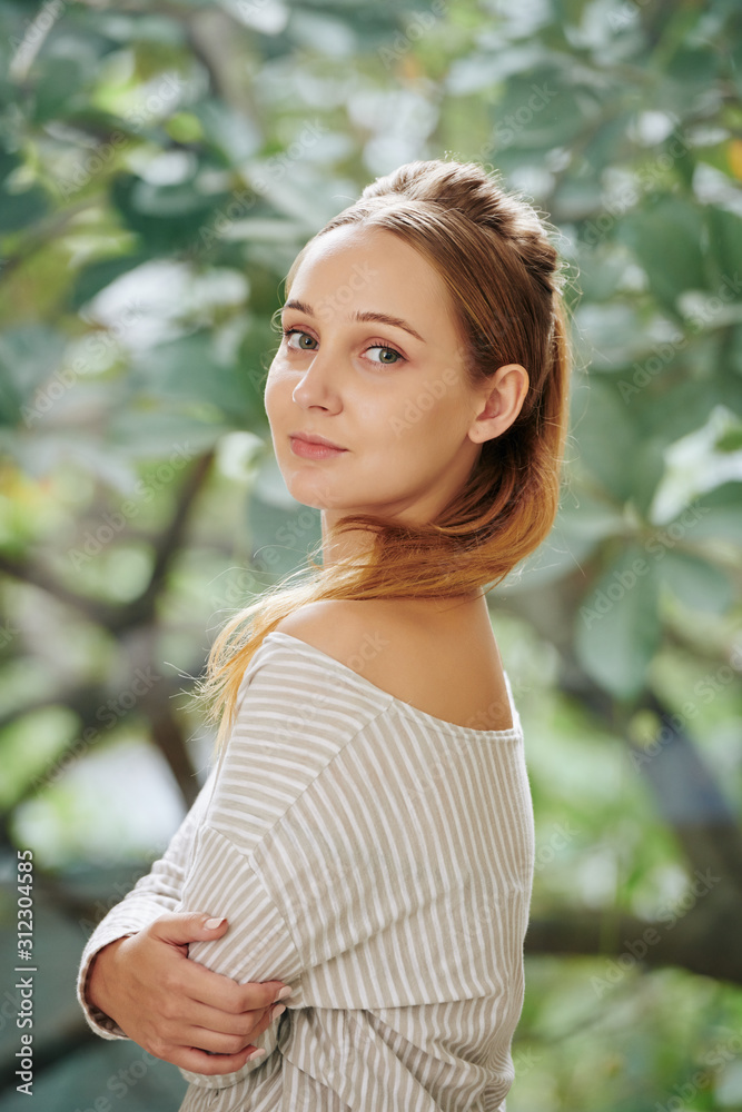 Beautiful charming young woman standing in garden and turning back to camera