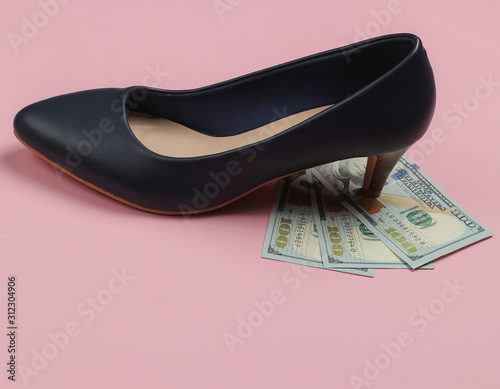 Femenism concept. Woman's high heel shoe stands on hundred-dollar bills on pink pastel background photo