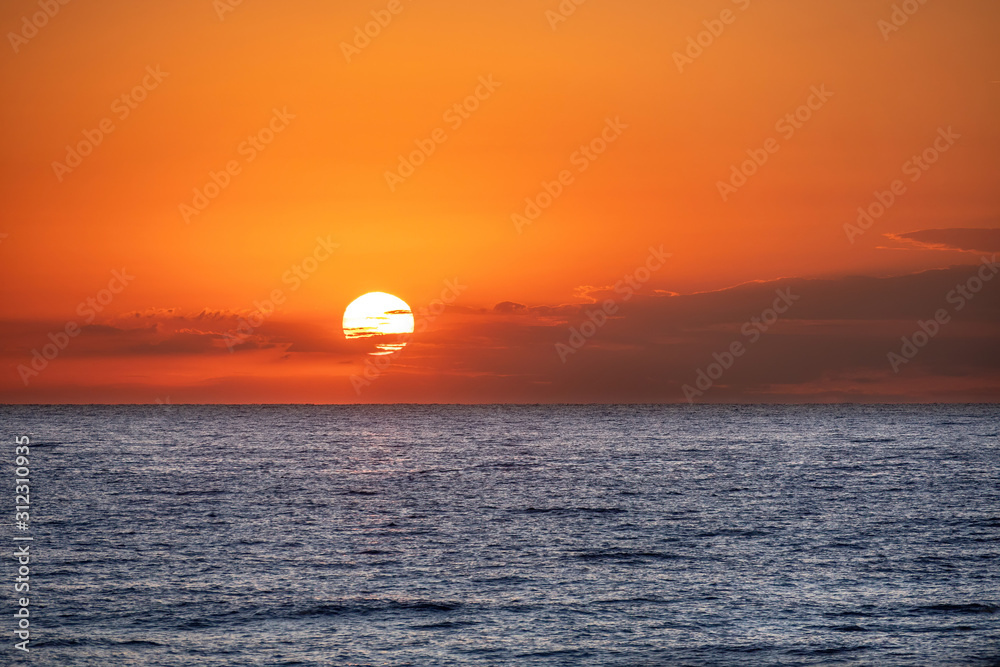 Orange sunrise above the calm blue sea. Sun shines in the clouds. Copy space.