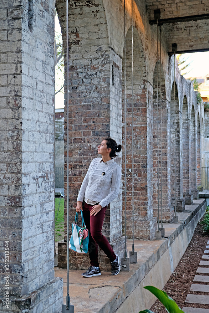 A young woman standing among the stone columns in Paddington Reservoir Gardens is an urban oasis in the city center in Sydney. It is a heritage-listed public park.