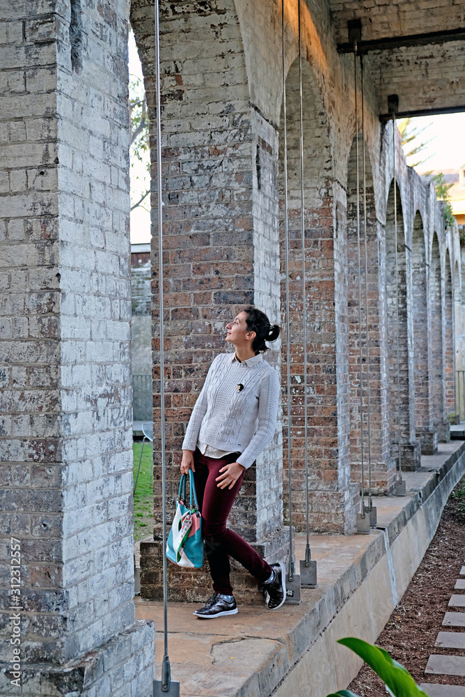A young woman standing among the stone columns in Paddington Reservoir Gardens is an urban oasis in the city center in Sydney. It is a heritage-listed public park.