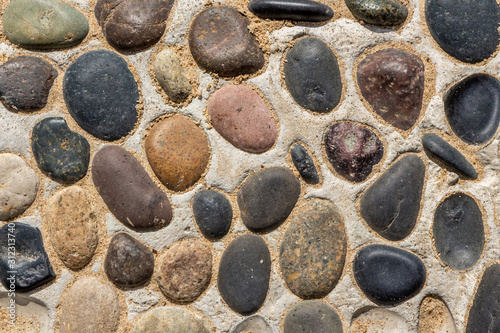Beautiful texture of path of gray and color smooth stones on the yellow background with sand is in the park