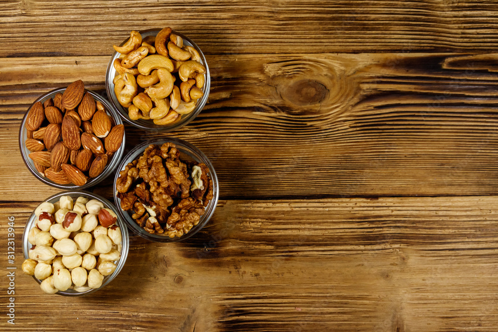 Assortment of nuts on wooden table. Almond, hazelnut, walnut and cashew in glass bowls. Top view, copy space. Healthy eating concept Assortment of nuts on wooden table. Almond, hazelnut, walnut and cashew in glass bowls. Top view, copy space. Healthy eating concept