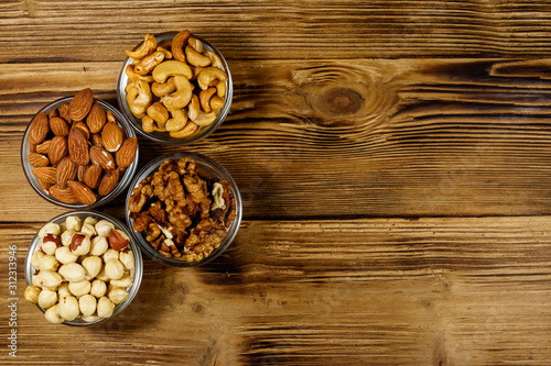 Assortment of nuts on wooden table. Almond, hazelnut, walnut and cashew in glass bowls. Top view, copy space. Healthy eating concept