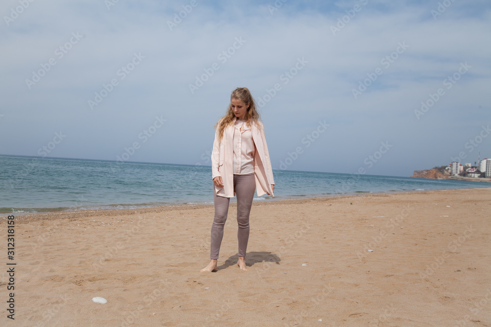 Beautiful blonde woman on an empty beach by the sea walks alone