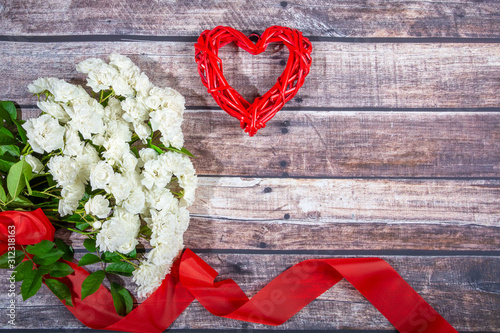 A bouquet of white roses with a red ribbon and rattan heart on a background of dark boards. Valentine's day, wedding, declaration of love. Place for text, top view, Copy Save, Flat Lay.